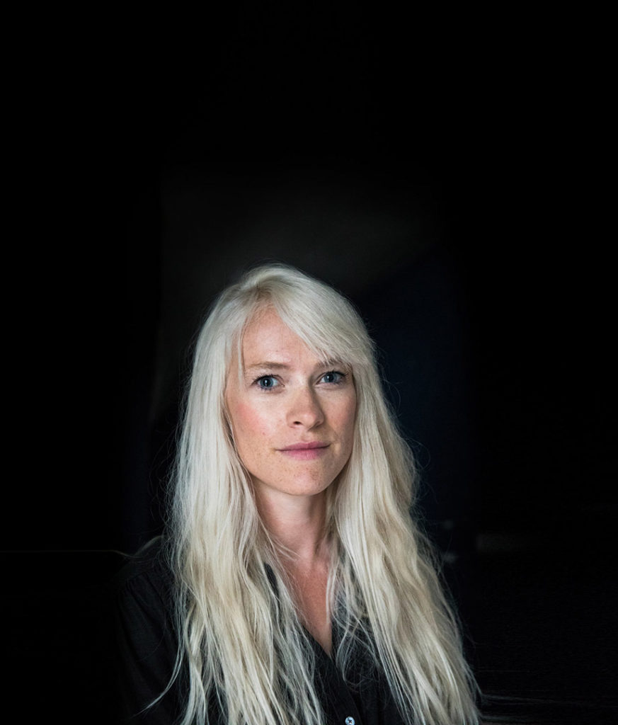 Portrait of Photojournalist Greta Rybus. The woman is looking into the camera, with blonde/platinum hair and a black top.