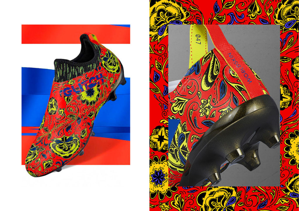 Vibrant designer soccer cleats with yellow, royal blue & black swirls on bright red. "Glitch" and "Worldskin" typography accents the heel and top.