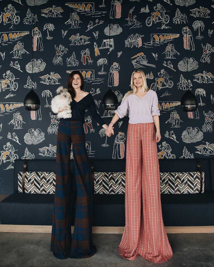 Creative portrait of She She, the collaborative between interior architect Jennifer Jorgensen and illustrator Kate Worum. Jorgensen and Worum standing in front of custom illustrated wallpaper.