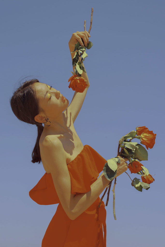 Creative, inspiring, landscape and nature photograph by Xuebing Du showing a woman holding roses and gently lifting them into the air while looking in the distance.