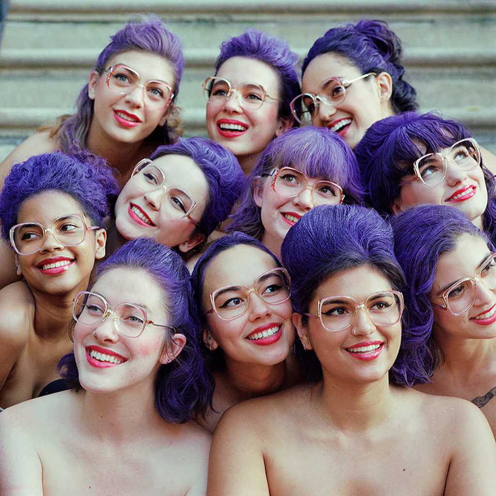 Expressive, group portrait of diverse women with matching makeup featuring red lips and purple hair. Shot by Sinjun Strom.